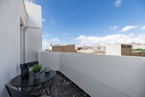 Terraço no telhado com mesa, cadeiras, um vaso de planta e vista para edifícios ao redor.