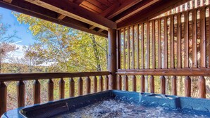 A hot tub with a wooden deck and railing, surrounded by trees. - Cozy Cabin with Amazing Views! Sleeps 8! Private Hot Tub! Resort Pools/Mini Golf (Sevierville)