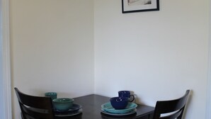 A dining area with a table and four chairs, a framed picture on the wall, and a door to the left.