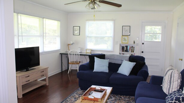 A living room with a TV on a wooden stand, a blue sofa, a coffee table, and a ceiling fan.