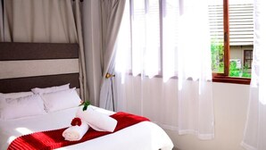 A neatly made bed with white linens and a red throw blanket, a wooden headboard, and a window with sheer curtains. - Novus Guest House (Pretoria)
