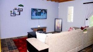 A living room with a beige sofa, a red rug, a television mounted on the wall, and a window with curtains. - Novus Guest House (Pretoria)