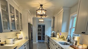 A modern kitchen with light blue cabinets, a central island, a chandelier, and a view to the dining area. - Cozy Modern Farmhouse (Port Matilda)
