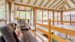 A spacious room with a wooden ceiling, large windows, a sofa, a table with a vase of flowers, and a wooden railing. - Modern Villa in the Sacred Valley: Sauna, Jacuzzi, views of the mountains and the Arin Waterfall. (Cuzco)