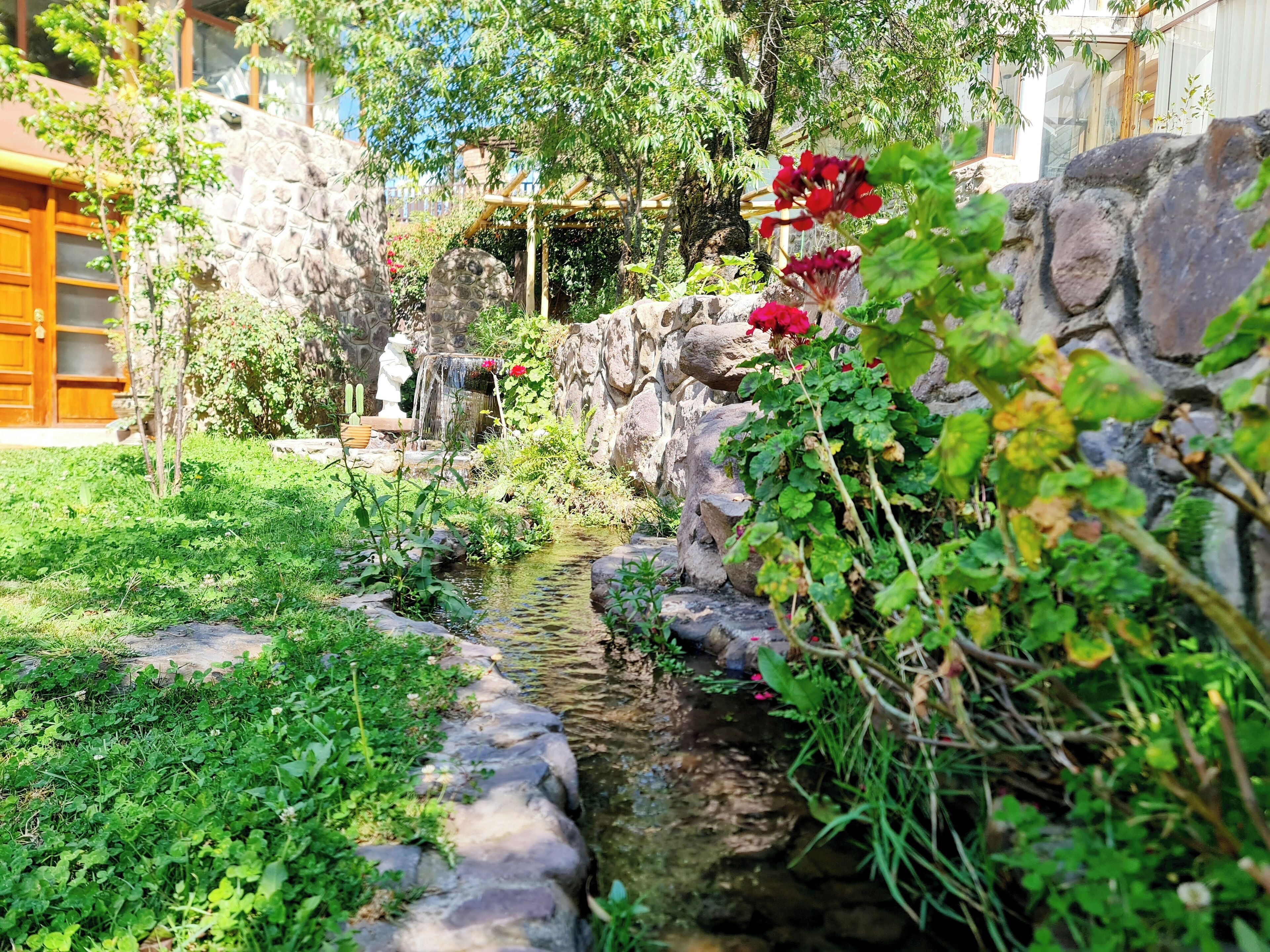 A garden with a small stream, stone walls, and a wooden pergola.