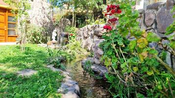 A garden with a small stream, stone walls, and a wooden pergola.