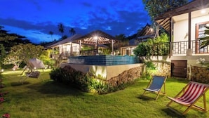 A well-lit outdoor area with a swimming pool, lounge chairs, and a covered seating area. - Luxury Beachfront Pool Villa - Finu@Samui (Koh Samui)