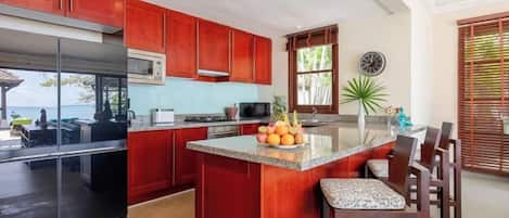 A kitchen with red cabinets, a large island, and a view to the outside.