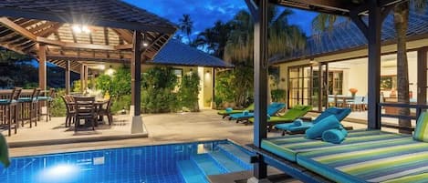 A pool area with lounge chairs, a covered seating area, and a view of the surrounding landscape.