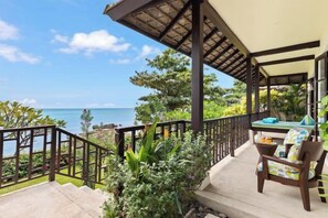 Un espace extérieur abrité avec vue sur la mer, une chaise en bois et une table avec des coussins.