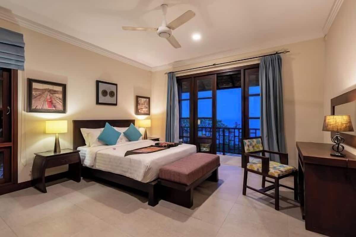 A hotel room with a bed, bedside tables, a desk, a chair, and a balcony with curtains.