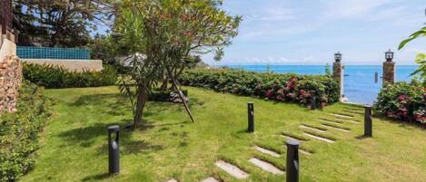 A well-maintained garden with a stone pathway leading to a view of the sea.