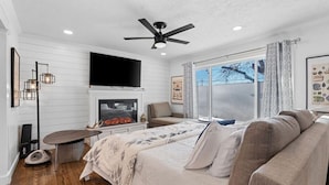Une chambre à coucher comprenant un lit, un canapé, une cheminée, un ventilateur de plafond et un téléviseur.