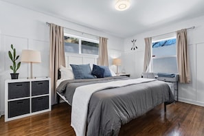 A bedroom with a bed, bedside tables, a potted plant, and a window with curtains.