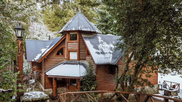 A wooden cabin with a sloped roof, a stone foundation, and a wooden porch. - BOG Torres del Bayo (Villa La Angostura)