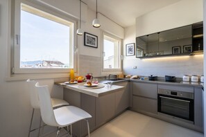 Et moderne køkken med et stort vindue, indbygget ovn og et spiseområde med en hvid stol.