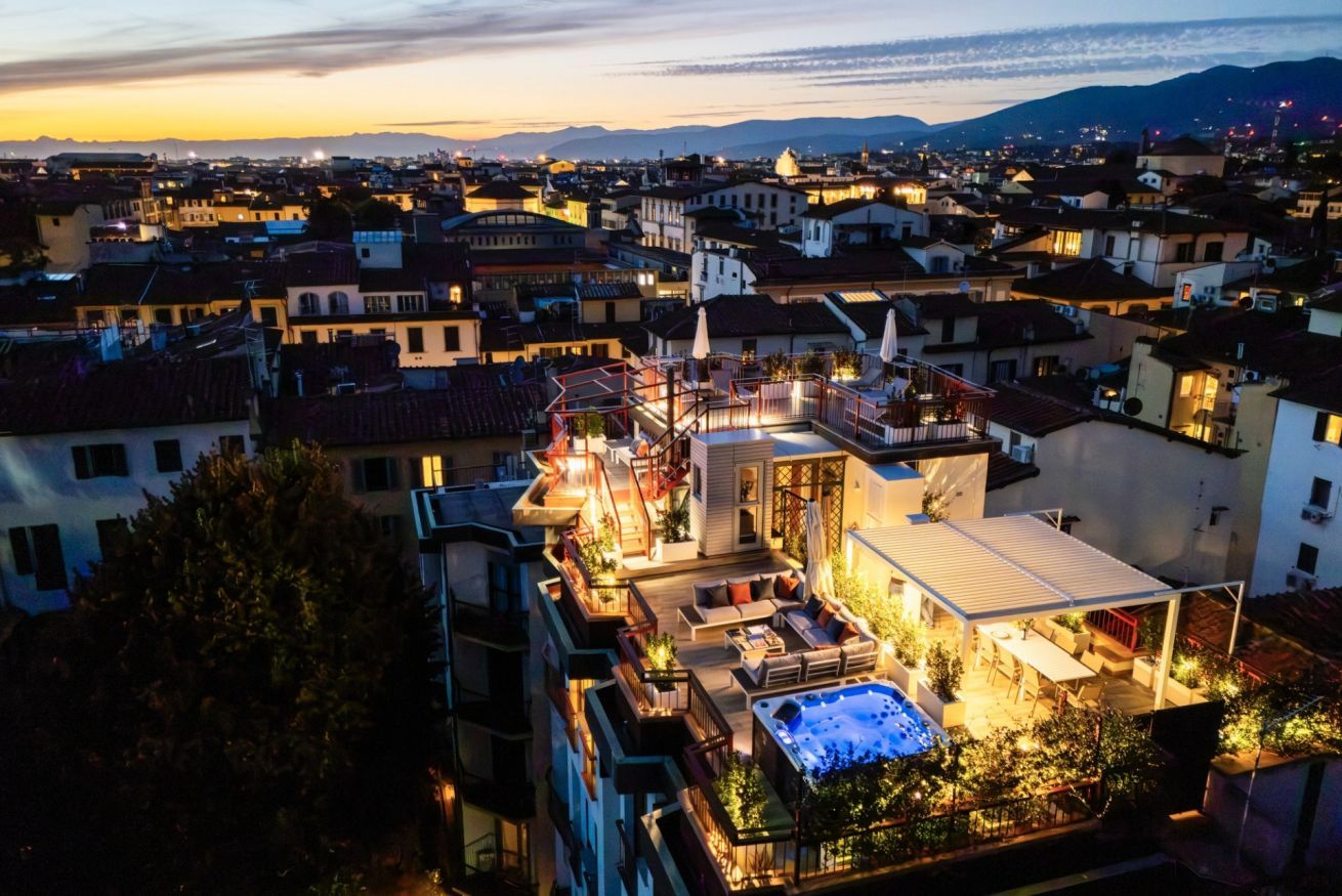 Eine Dachterrasse mit Whirlpool, Sitzgelegenheiten im Freien und Blick auf eine Stadtlandschaft im Abenddämmerung.