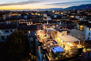 A rooftop with a hot tub, outdoor seating, and a view of a cityscape at dusk.