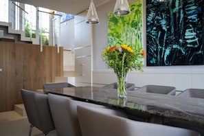 A modern dining area with a marble table, grey chairs, a vase with flowers, and abstract art on the wall.