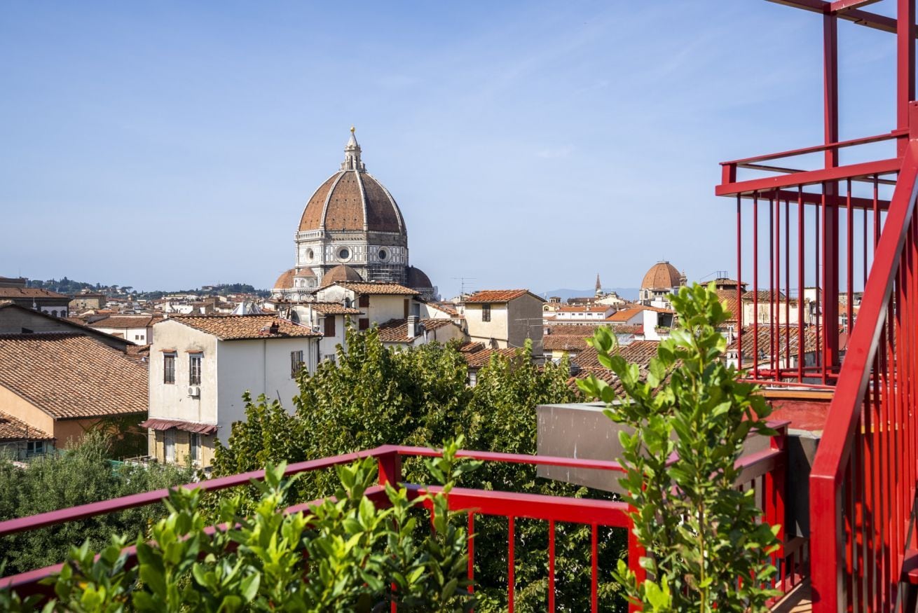 Un bâtiment en forme de dôme, avec une balustrade rouge au premier plan, entouré de verdure et d’autres bâtiments.