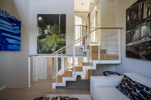Et moderne interiør med trappe, hvid sofa og billedkunst på væggene.