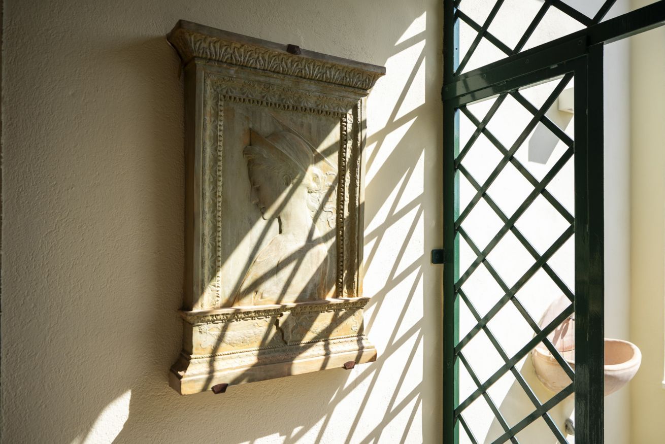 Eine Wandskulptur mit klassischem Design, ein Metallgitter und ein Blumentopf.