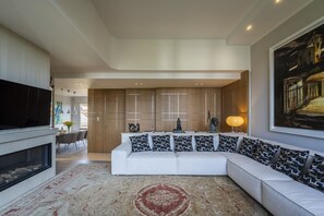 A modern living room with a white sofa, patterned cushions, a fireplace, and a large painting on the wall.
