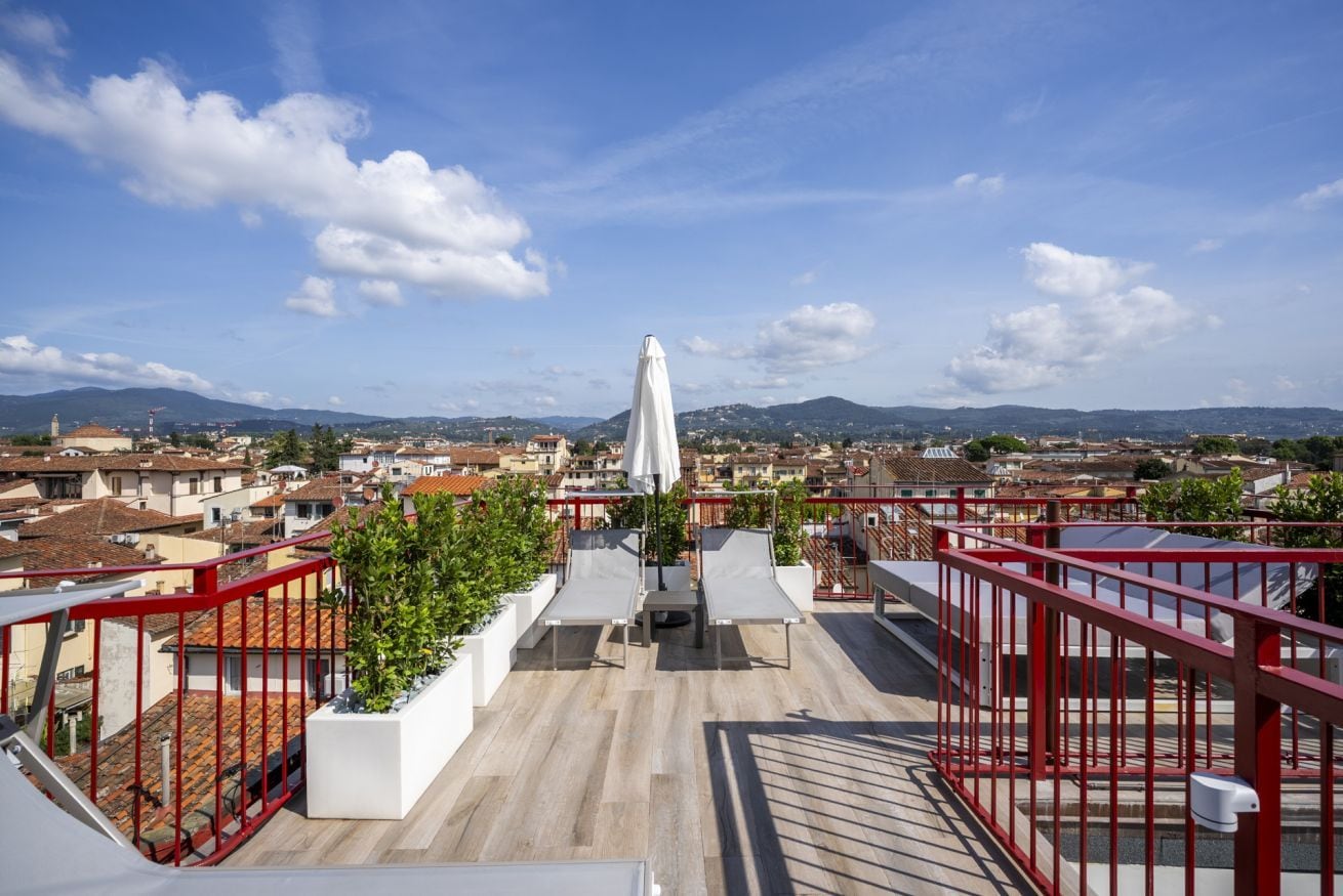 Eine Dachterrasse mit Liegestühlen, einem weißen Sonnenschirm und einem roten Geländer.