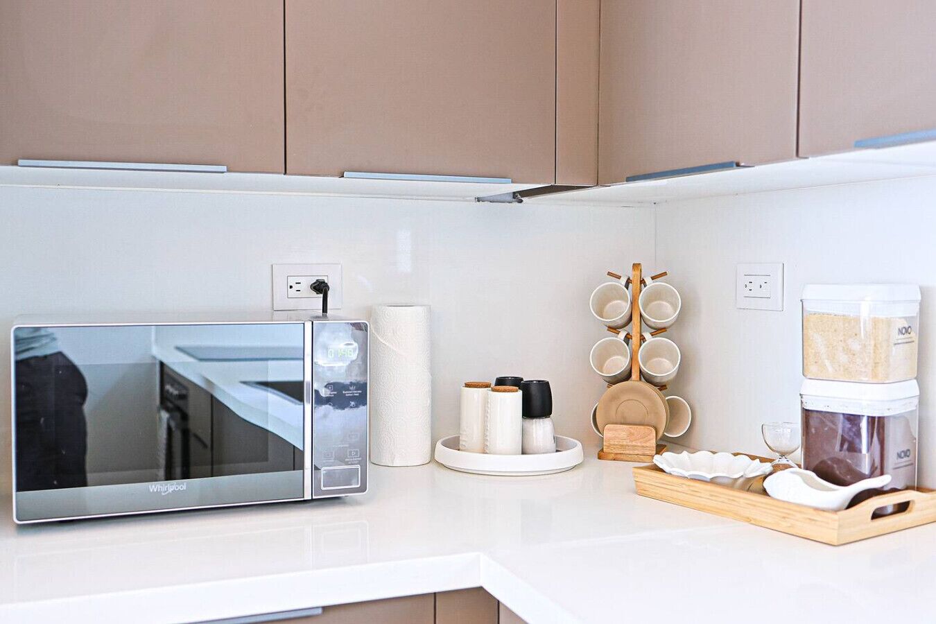 A kitchen with a built-in microwave, a paper towel dispenser, a wooden utensil holder, and a coffee maker.