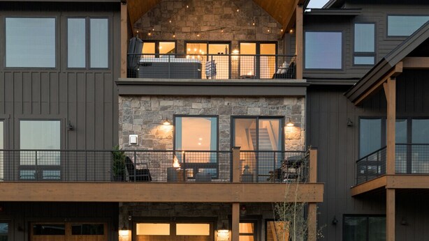A modern multi-story house with a stone facade, large windows, and a covered balcony.