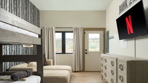 A bedroom with bunk beds, a television, a dresser, and a window with curtains.