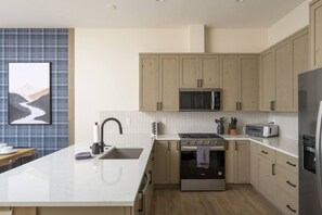 A modern kitchen with a central island, stainless steel appliances, and light-colored cabinetry. - Lodge 212 | Brand New LUXE Designer Home + Hot Tub (Fraser)