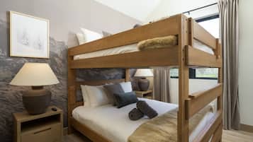 A bunk bed with a wooden frame, two bedside tables with lamps, a framed picture on the wall, and a window with curtains.