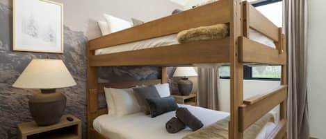 A bunk bed with a wooden frame, two bedside tables with lamps, a framed picture on the wall, and a window with curtains.