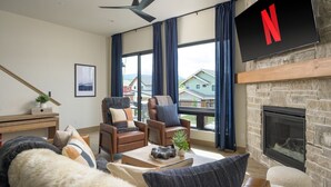 A modern living room with a fireplace, two leather armchairs, a sofa, and a TV mounted on the wall.