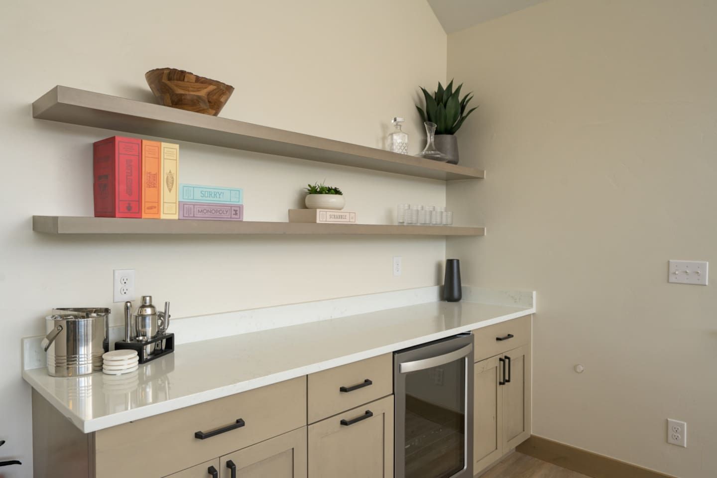 Une cuisine avec un plan de travail blanc, des armoires de couleur beige et un four encastré. Des étagères au-dessus du plan de travail servent à ranger des livres et des objets décoratifs.