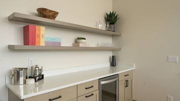 A kitchen with a white countertop, beige cabinets, and a built-in oven. There are shelves above the counter holding books and decorative items.
