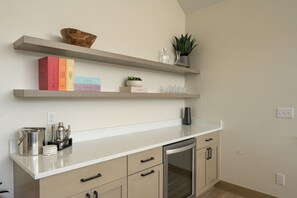 A kitchen with a white countertop, beige cabinets, and a built-in oven. There are shelves above the counter holding books and decorative items.