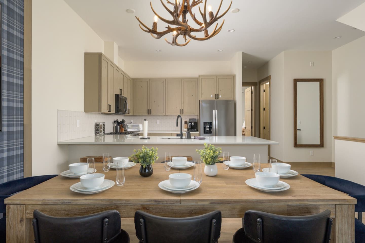 Une cuisine moderne dotée d’un îlot central, d’appareils électroménagers en acier inoxydable et d’un coin repas avec une table en bois prévue pour accueillir six personnes.