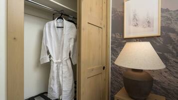 A wooden door leading to a closet with a white robe hanging, a lamp on a bedside table, and a framed picture on the wall.