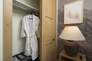 A wooden door leading to a closet with a white robe hanging, a lamp on a bedside table, and a framed picture on the wall.