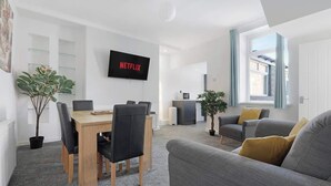 Ein modernes Wohnzimmer mit Essbereich, einem Flachbildfernseher und Blick ins Freie.
