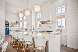 Une cuisine spacieuse dotée d’un grand îlot central, de meubles blancs et de luminaires suspendus.
