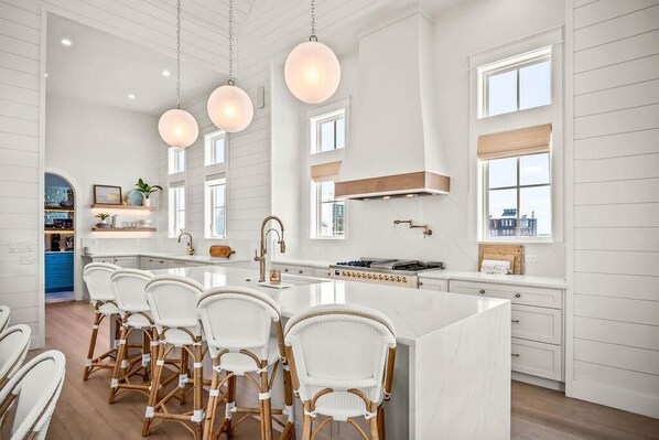 A spacious kitchen with a large island, white cabinetry, and pendant lighting.