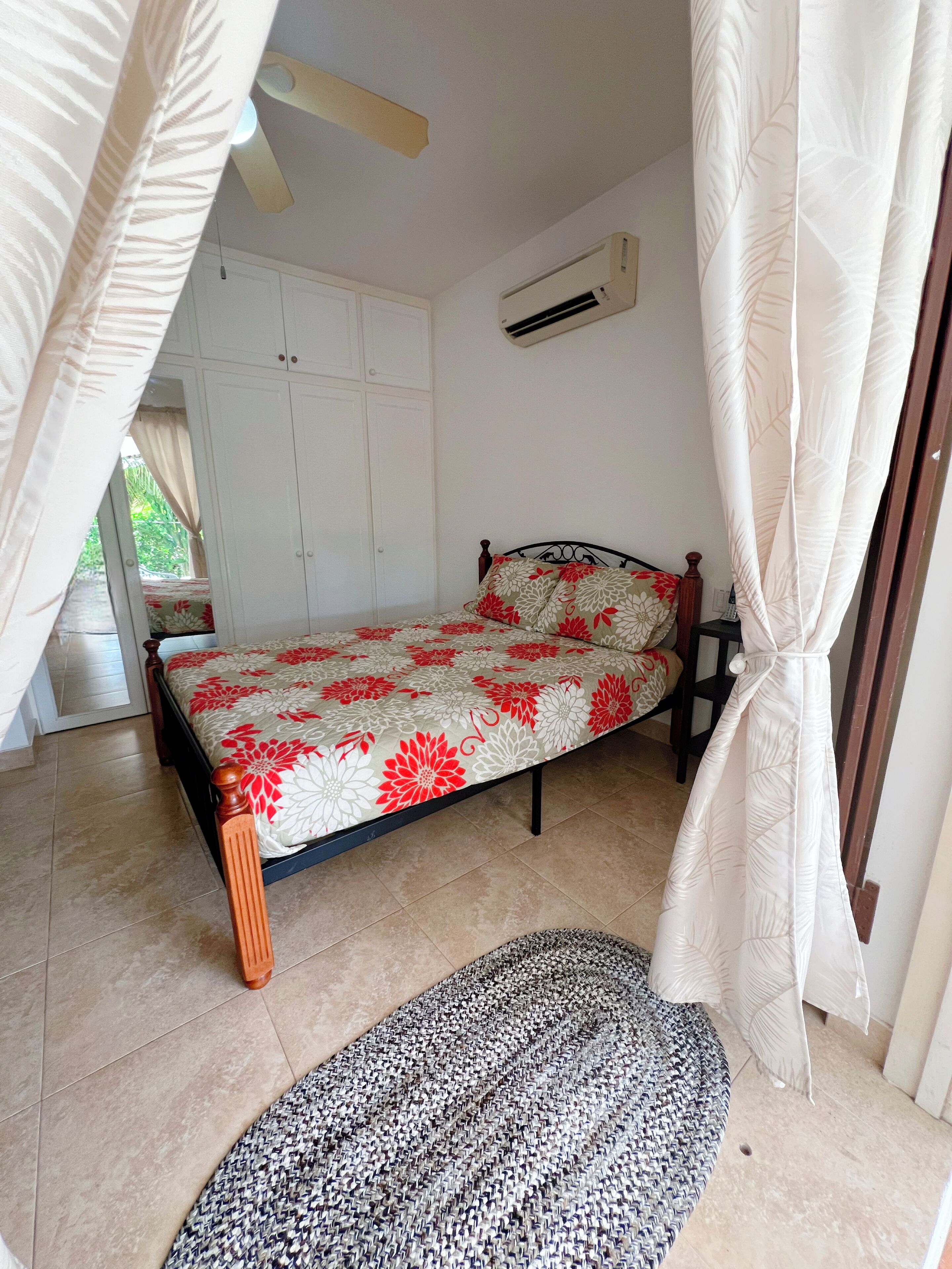 A bedroom with a bed, a wardrobe, an air conditioning unit, and a patterned rug.