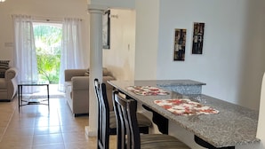 Une cuisine moderne avec un comptoir en granit, des chaises en bois foncé et une table à manger. Une fenêtre avec des rideaux blancs offre une vue sur la verdure à l’extérieur.
