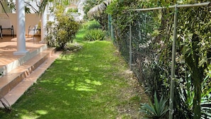 Un jardin bien entretenu, agrémenté d’un sentier, de palmiers et d’un bâtiment blanc orné d’arcades.