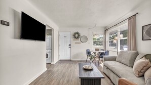 A modern living room with a flat-screen TV, a sofa, a coffee table, and a dining area with chairs and a table.
