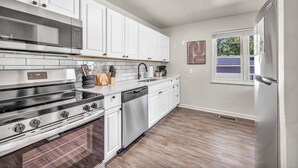A modern kitchen with white cabinets, stainless steel appliances, and a window with blinds.