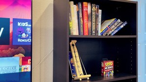 A room with a television displaying a children's show, a bookshelf with books and a game, and a neon sign reading "CINEMA". - Getaway Spot Close to Red Rocks, Denver, Mtns (Lakewood)